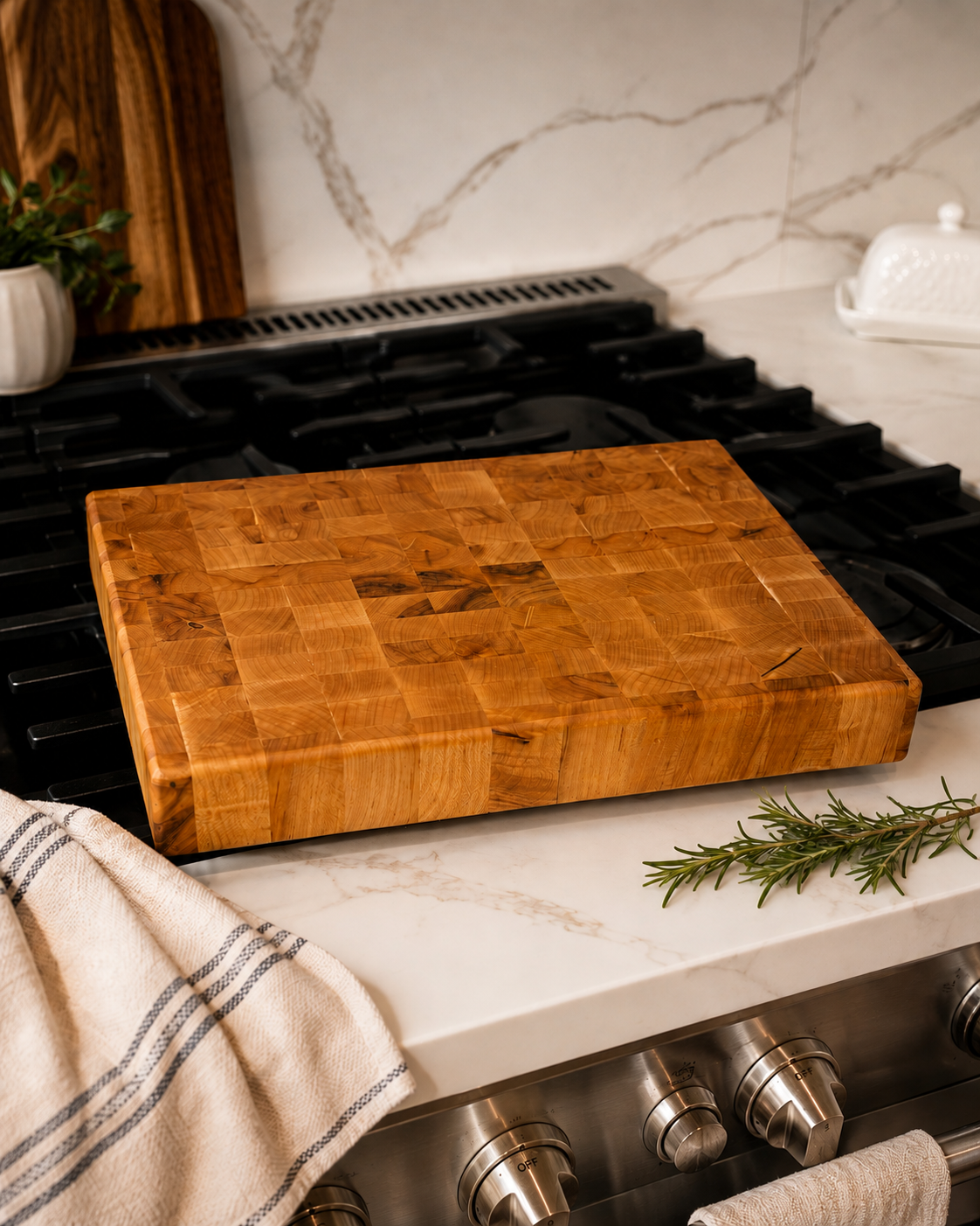End grain cutting board on marble countertop next to a gas stove with fresh rosemary
